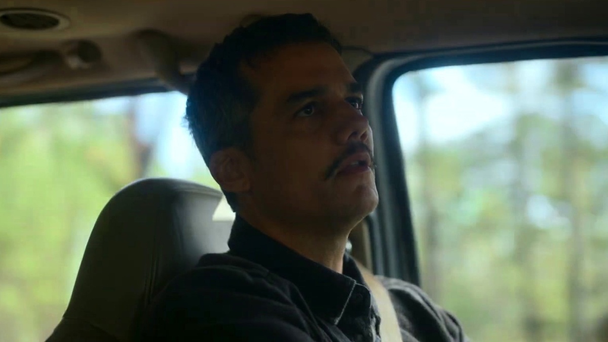 Wagner Moura, com bigode e camisa escura, dirige um carro, olhando para frente com expressão séria. Cena do filme Guerra Civil (2024).