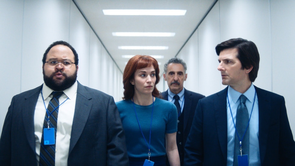 Onde assistir às séries vencedoras do Emmy 2025 2 Mark Scout (Adam Scott), Helly (Britt Lower), Irving (John Turturro) e Dylan (Zach Cherry) caminham juntos por um corredor branco e iluminado na série Ruptura (Severance), da Apple TV+.