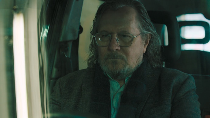 Onde assistir às séries vencedoras do Emmy 2025 3 Jackson Lamb (Gary Oldman) aparece sentado em um carro, com expressão séria e usando óculos, na série Slow Horses, da Apple TV+.
