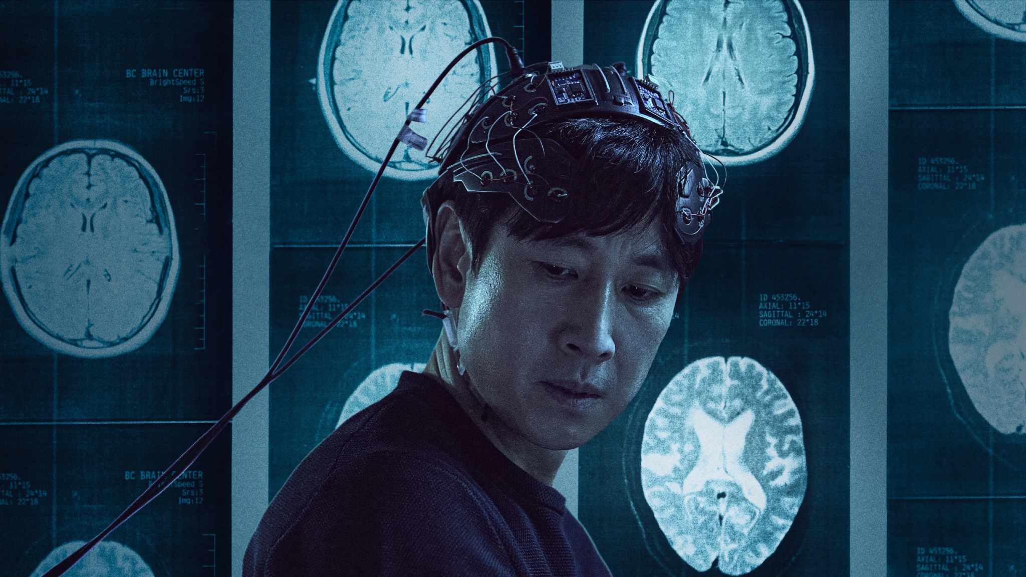 Cena de Dr. Brain (2021–) mostra um cientista usando um capacete com fios conectados, com imagens de tomografias cerebrais exibidas ao fundo.