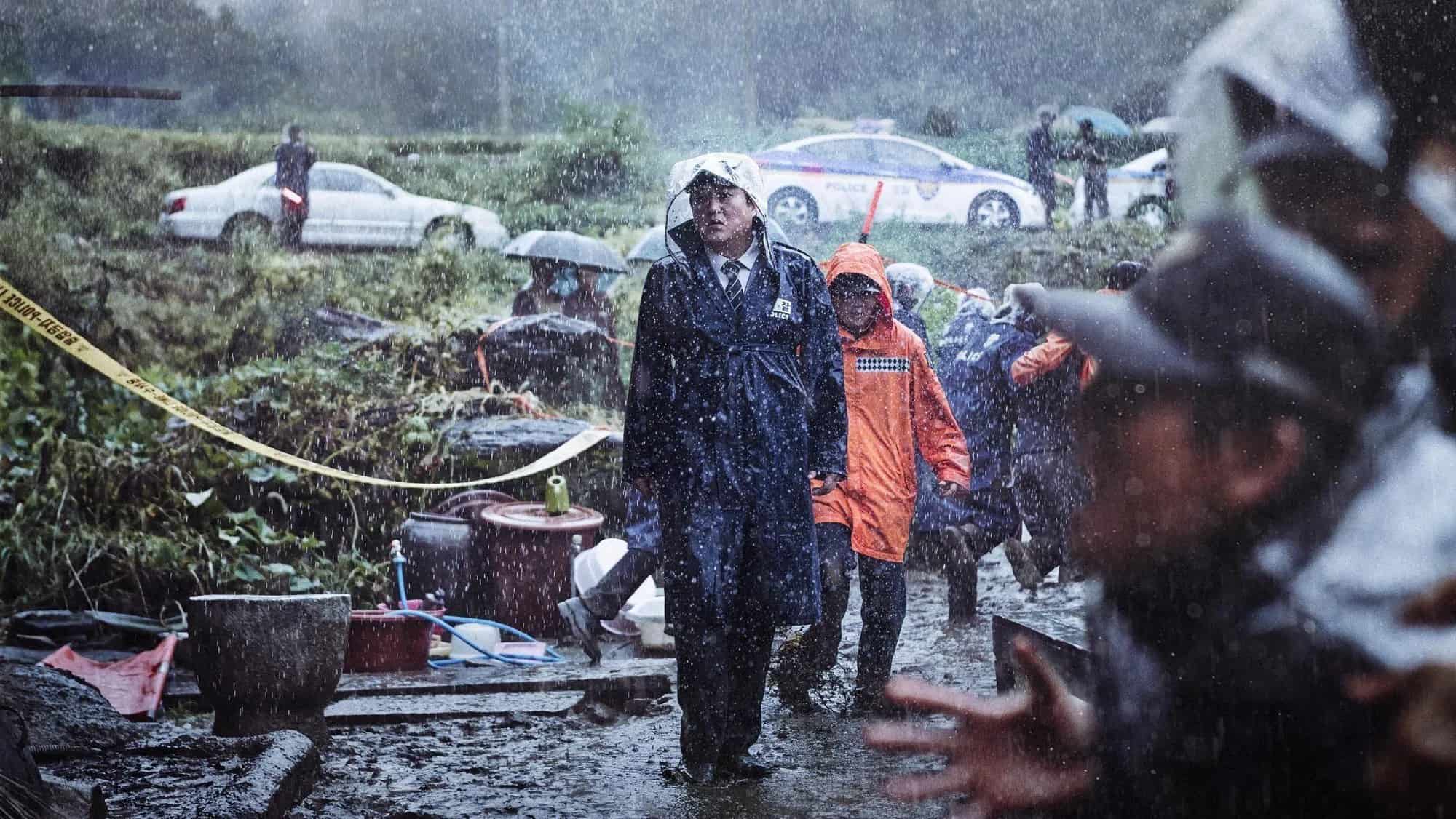 Filmes de terror asiáticos famosos: 12 obras que conquistaram o mundo 8 policial caminha sob forte chuva em área isolada cercada por fitas de investigação, enquanto moradores observam ao redor.