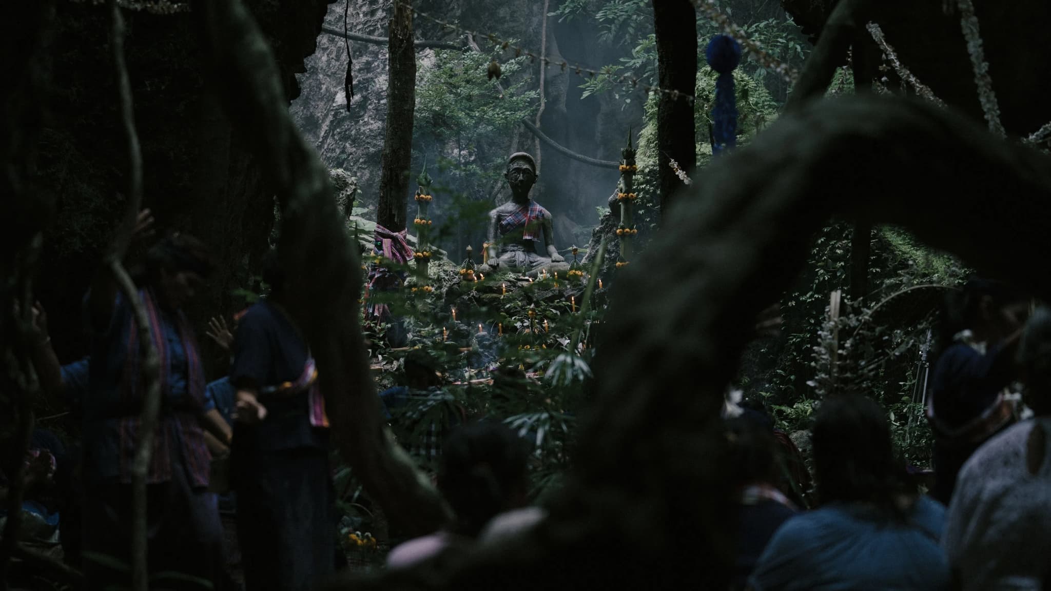Filmes de terror asiáticos famosos: 12 obras que conquistaram o mundo 9 grupo de pessoas realiza um ritual em meio a uma floresta densa, com uma estátua envolta por oferendas no centro.