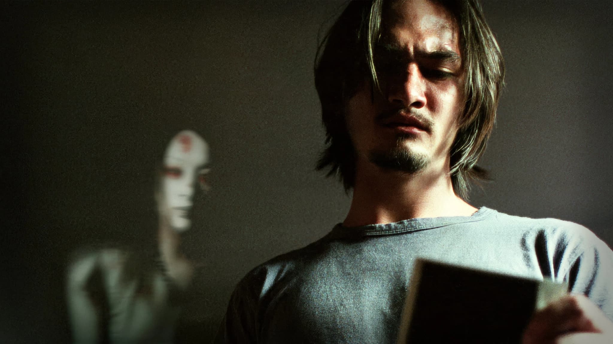 Filmes de terror asiáticos famosos: 12 obras que conquistaram o mundo 10 homem observa uma fotografia com expressão de dúvida enquanto uma figura fantasmagórica aparece desfocada ao fundo.