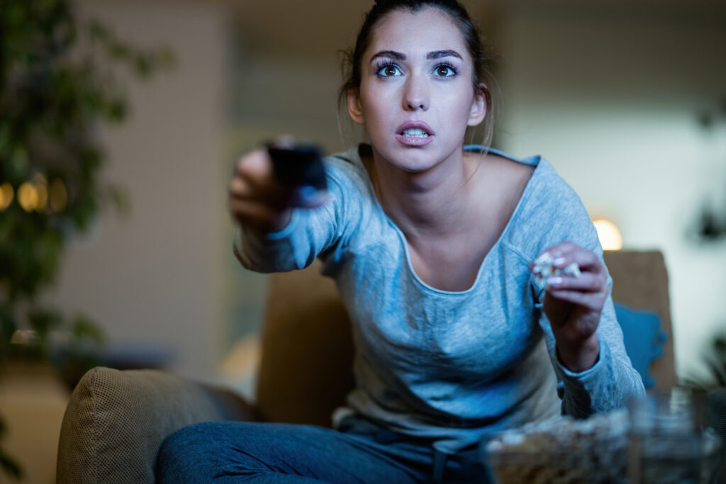 O impacto da exploração de cenários na evolução da cultura pop 1 young woman sitting dark changing channels tv while eating popcorn home