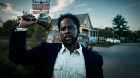 Harold Perrineau como Boyd Stevens em cena da série Origem segurando um sino em estrada deserta