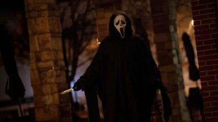 Ghostface usando o uniforme preto e a máscara branca em cena gravada na rua